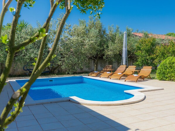 A swimming pool with wooden lounge chairs and a pergola.