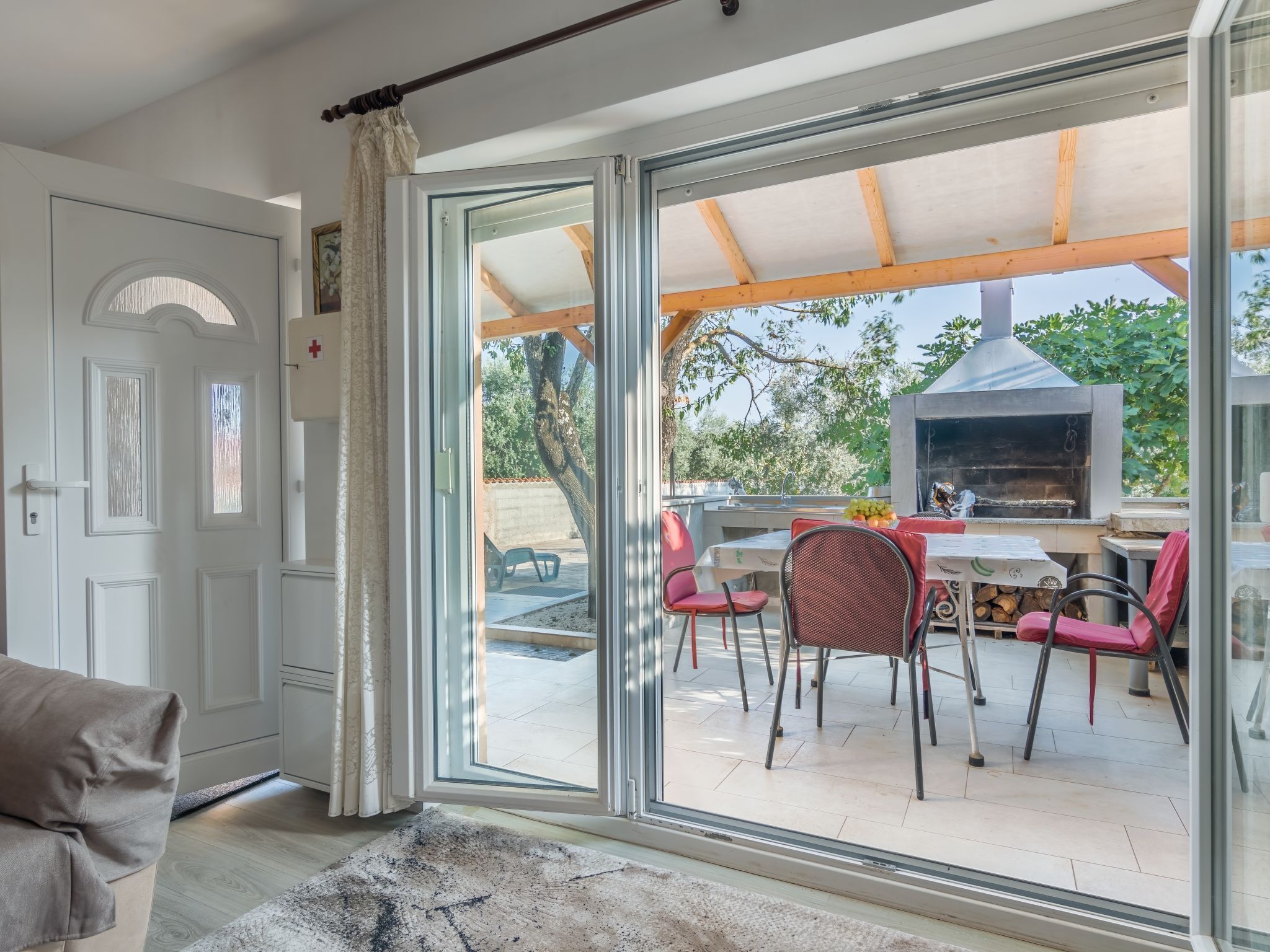 Een modern interieur met een schuifglazen deur naar een terras met een pizzaoven, eettafel en stoelen.