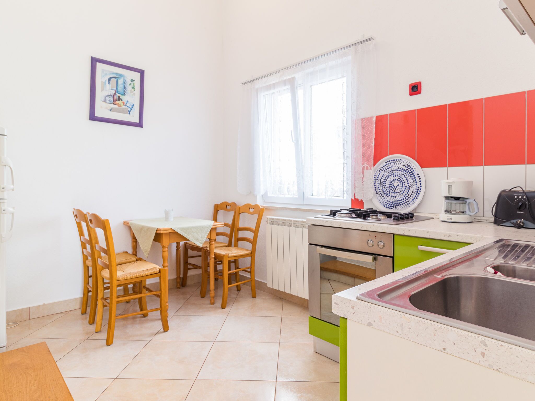 A compact kitchen with a dining table, chairs, a stove, a sink, and a window with curtains.