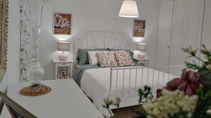 A bedroom with a white bed, two bedside tables with lamps, floral artwork on the walls, and a white wardrobe.