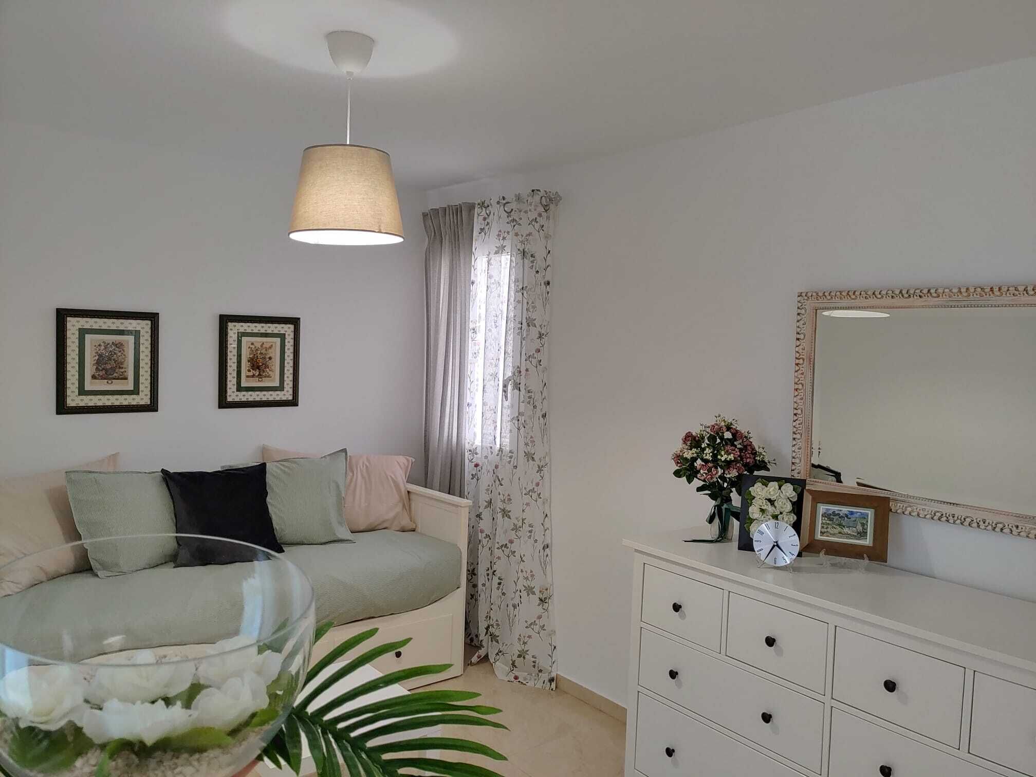 Une chambre à coucher avec un lit, une commode, un miroir et une fenêtre avec des rideaux.