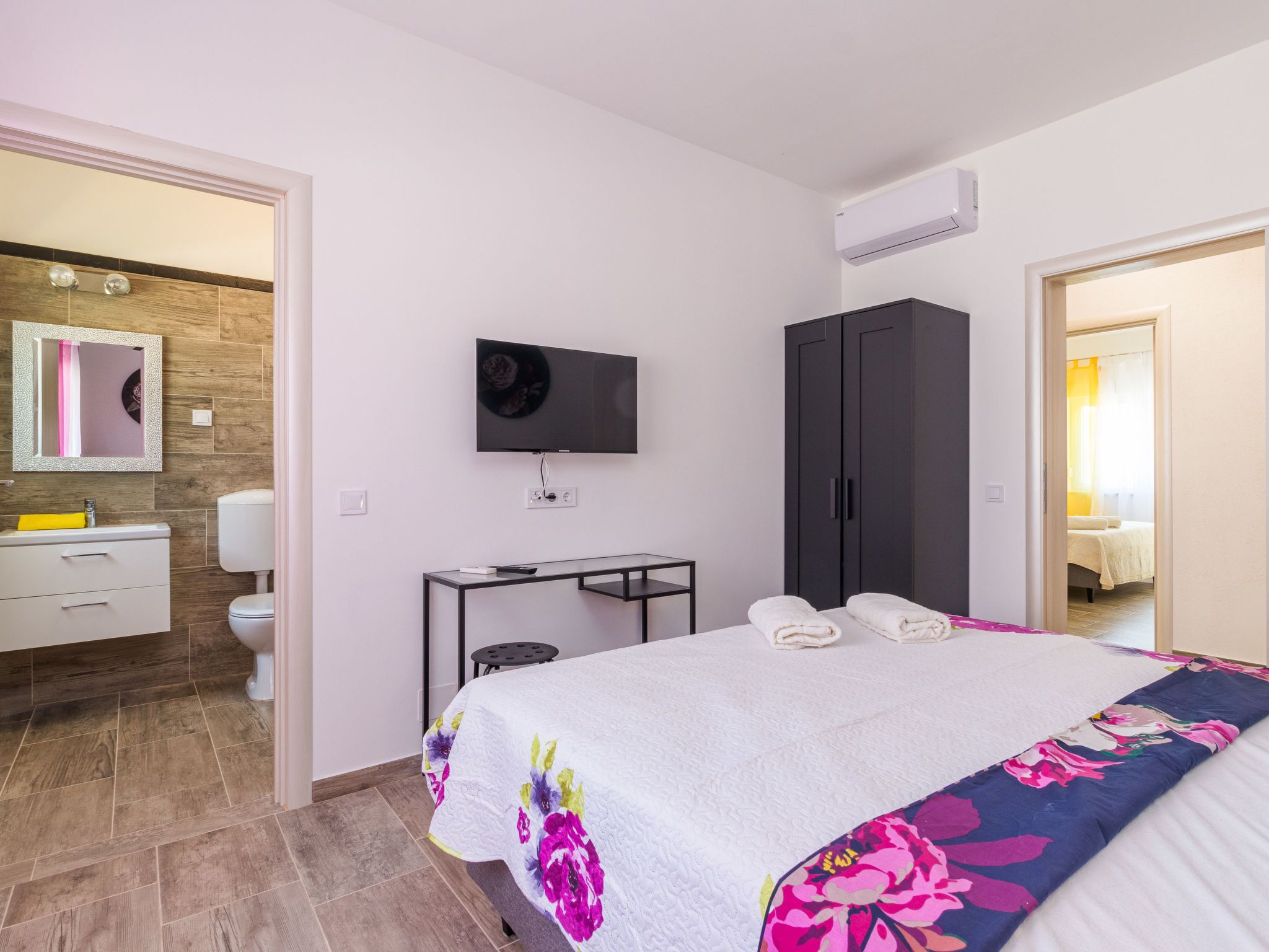 Habitación de hotel con cama, televisión, armario, escritorio y baño con espejo y lavabo.