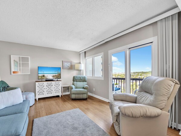 A spacious living area with a large window, a sofa, a chair, and a television.