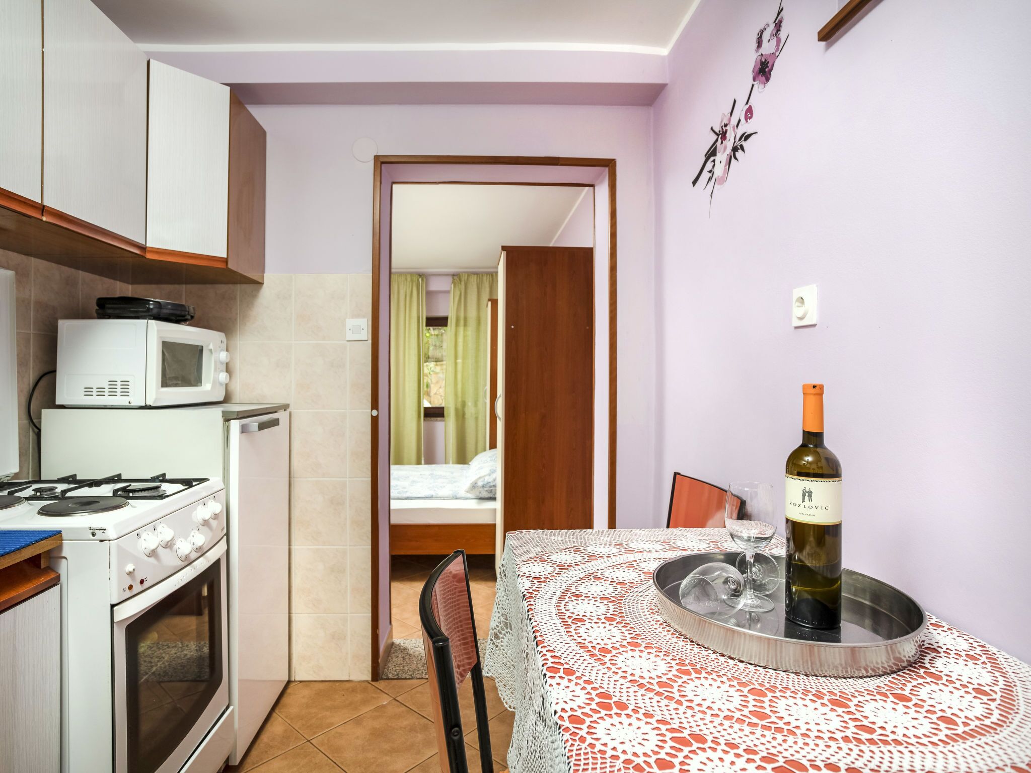 Une cuisine compacte équipée d’une cuisinière, d’un four à micro-ondes et d’un four traditionnel. On aperçoit une table à manger avec une bouteille de vin et des verres.