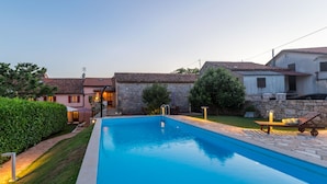 Una piscina con borde de piedra, rodeada por un césped cuidado y un muro de piedra.