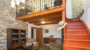 Amplia sala de estar con escalera de madera, paredes de piedra y mobiliario tradicional.