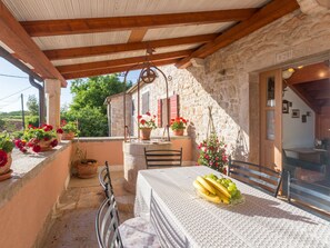 Un edificio in pietra con un balcone, un tavolo coperto da una tovaglia, sedie e vasi con fiori.
