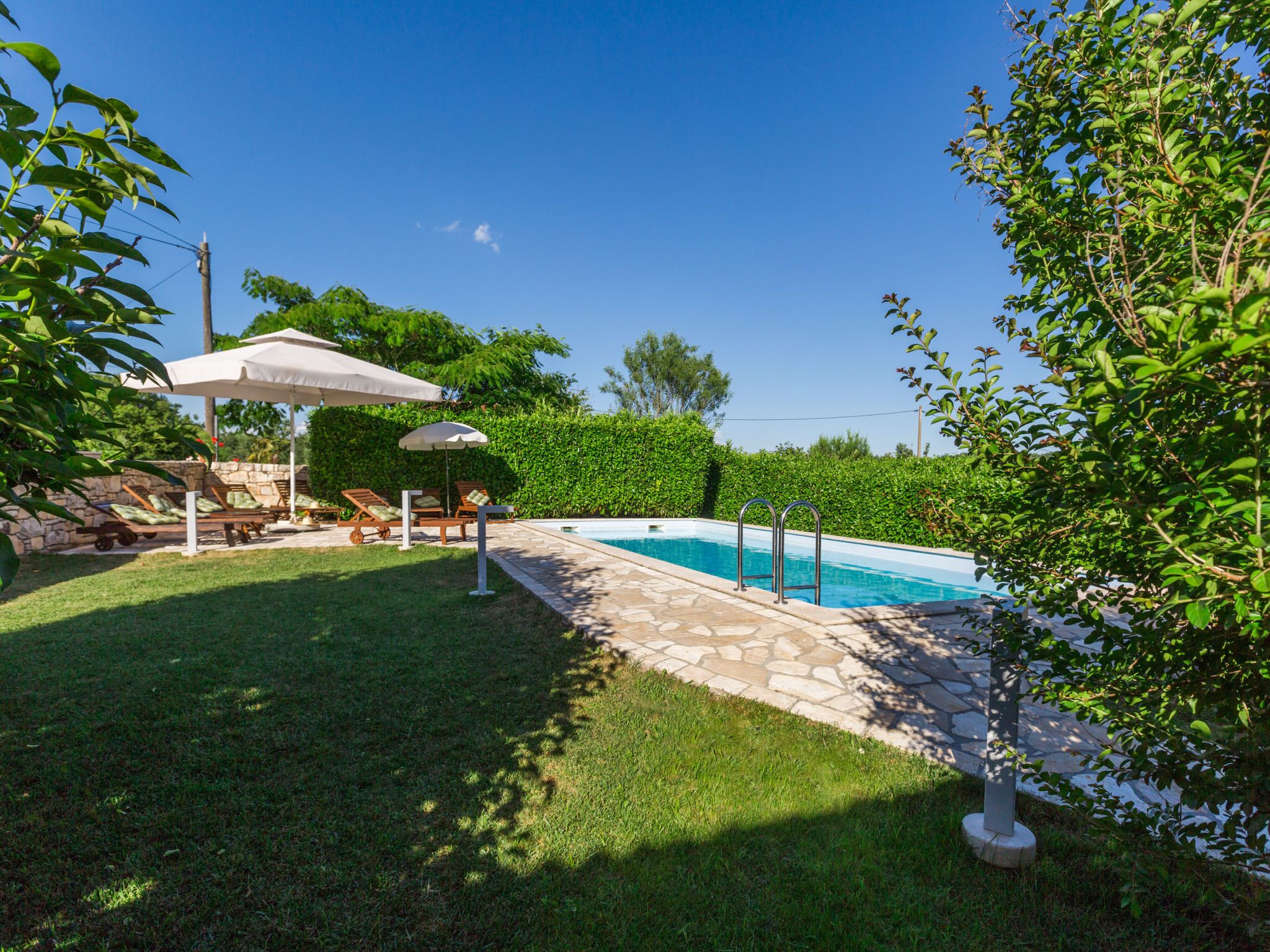 Una piscina con bordo in pietra, circondata da un'area verde e da un'area salotto coperta con ombrelloni.