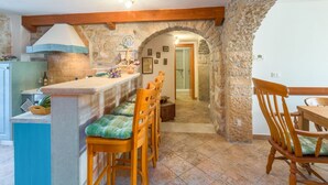 Una cocina rústica con paredes de piedra, sillas de madera y suelo de baldosas.