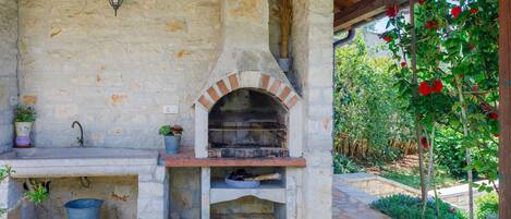 An outdoor stone oven with a brick arch, a sink, and potted plants.