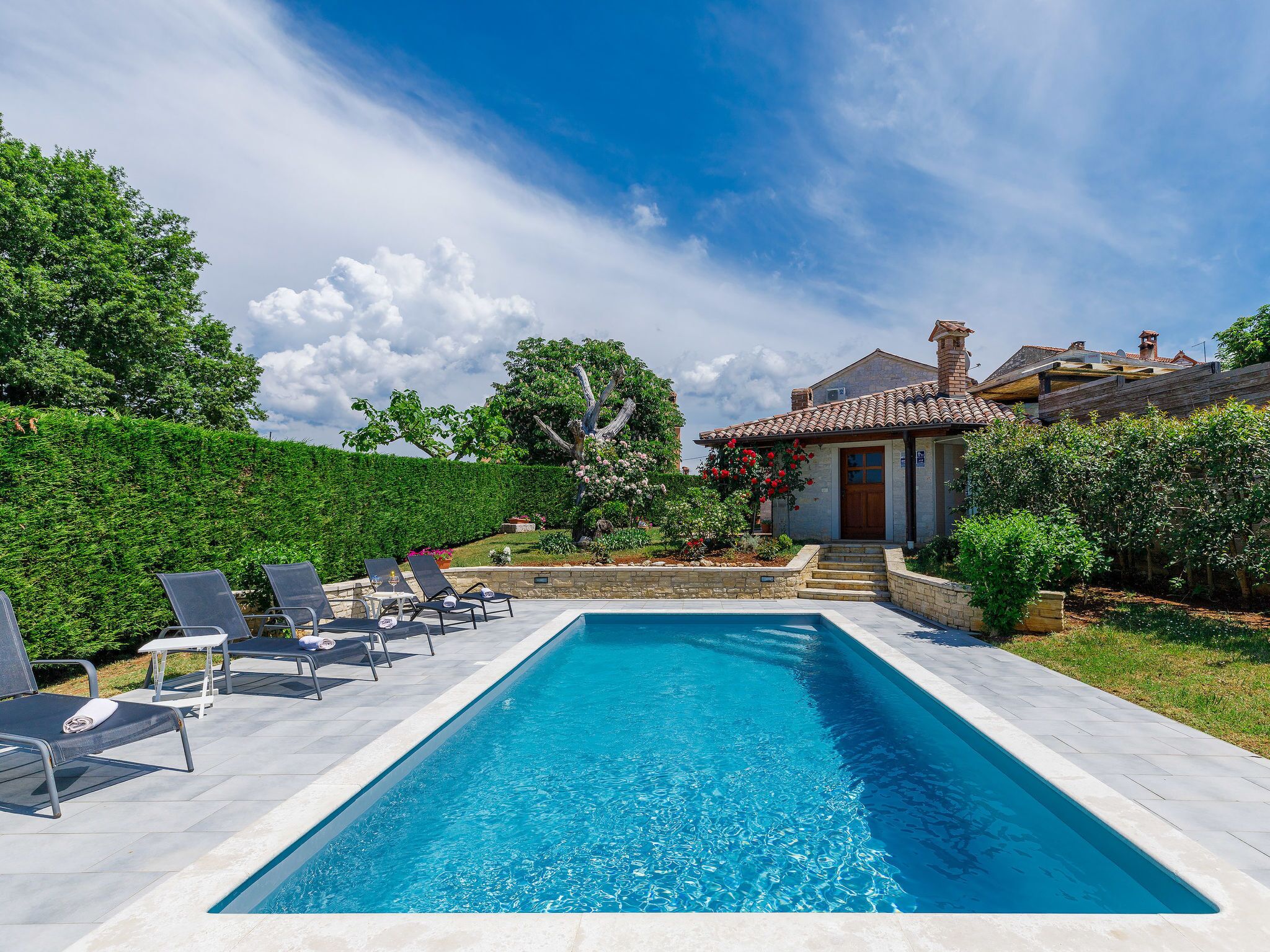 A swimming pool with lounge chairs, a house with a tiled roof, and a well-maintained garden.