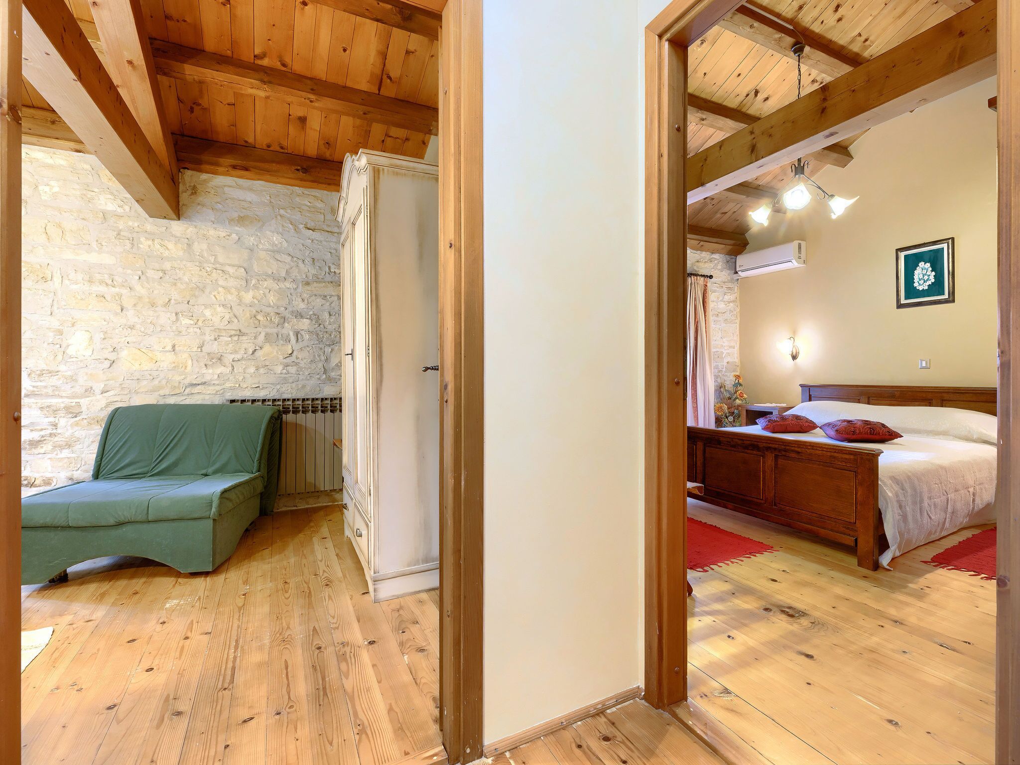 A bedroom with a wooden ceiling, a stone wall, and a bed with red pillows.