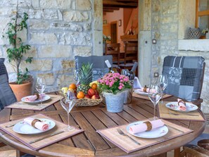 A wooden table set for dining with a stone wall backdrop, a potted plant, and a metal bucket with flowers. - Villa Dina by Interhome (Poreč)