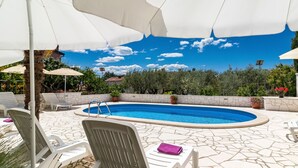 A swimming pool with lounge chairs and umbrellas, surrounded by greenery and a clear sky. - Apartment Koštro by Interhome (Poreč)