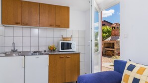 A compact kitchen with wooden cabinets, a microwave, and a sink. There's a basket of fruit on the counter and a blue sofa with a patterned cushion. - Apartment Koštro by Interhome (Poreč)