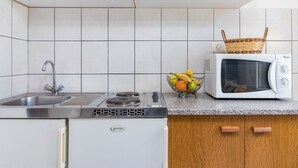 A kitchen with white cabinets, a stainless steel sink, a white refrigerator, a microwave, and a fruit basket on the counter. - Apartment Koštro by Interhome (Poreč)