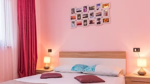 A neatly arranged bedroom with a large bed, two bedside tables, a wall of photos, and a window with curtains.