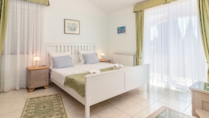 Une chambre à coucher avec un lit blanc, deux tables de chevet, un tapis à motifs verts et un luminaire au plafond.