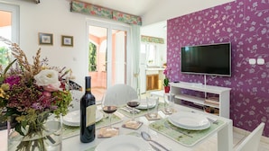 Un coin repas avec une table dressée pour deux personnes, une bouteille de vin et un vase de fleurs.