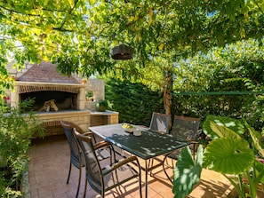 Enjoy dining and socializing in this serene outdoor patio area with a barbecue grill, metal table, and wicker chairs.
