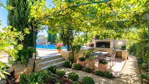 En terrasse med pool, udendørs møbler og en pejs af sten.