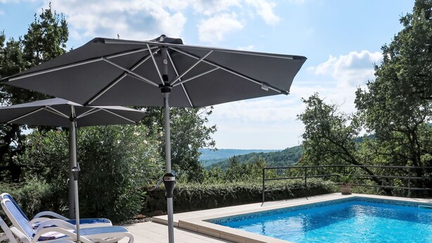 A poolside area with lounge chairs and an umbrella, surrounded by greenery and a view of hills. - Vacation home Mariva by Interhome (Pićan)