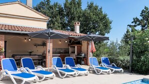 A swimming pool with lounge chairs and umbrellas, a barbecue area, and a brick house with a tiled roof. - Vacation home Mariva by Interhome (Pićan)