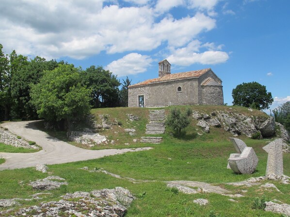 A stone building with a tiled roof, surrounded by a grassy area with a winding path leading to it.