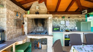 A rustic outdoor kitchen with a stone wall, a wood-fired oven, and a small kitchen area with a microwave and storage cabinets. - Apartment Pina by Interhome (Pazin)
