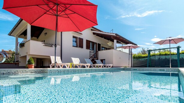 Une piscine avec un sol carrelé, des chaises longues et des parasols.