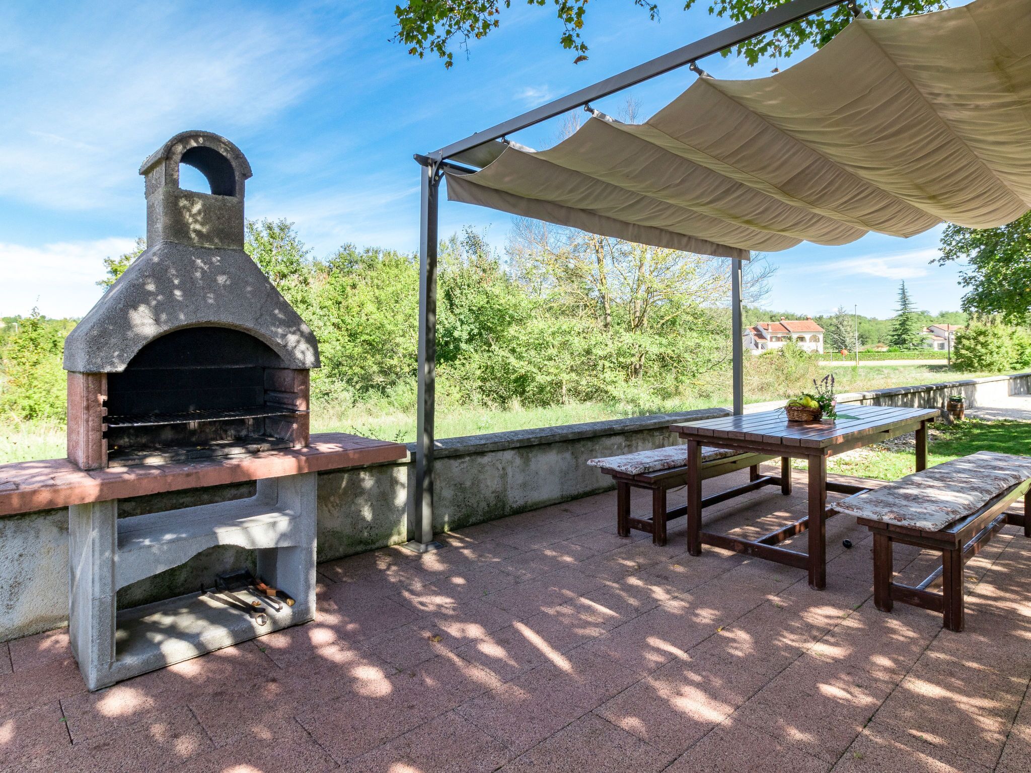 Patio esterno con forno a legna in pietra, tavolo coperto e panche.