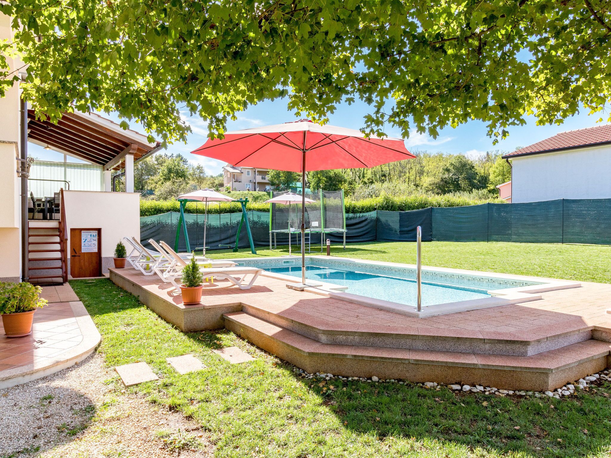 A backyard with a swimming pool, a covered seating area, and a staircase leading to a patio.