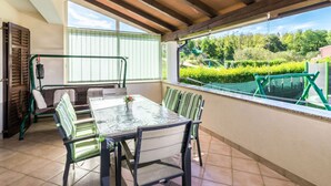 Une terrasse couverte avec une table et des chaises, une vue sur la verdure et un plafond en bois.
