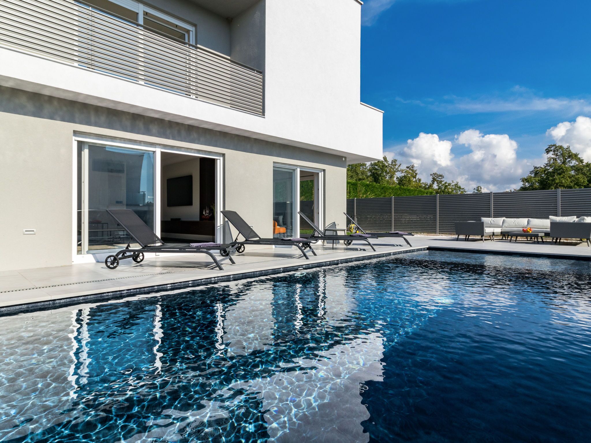 Ein moderner Poolbereich im Freien mit Liegestühlen und einem Eingang mit Glastür.