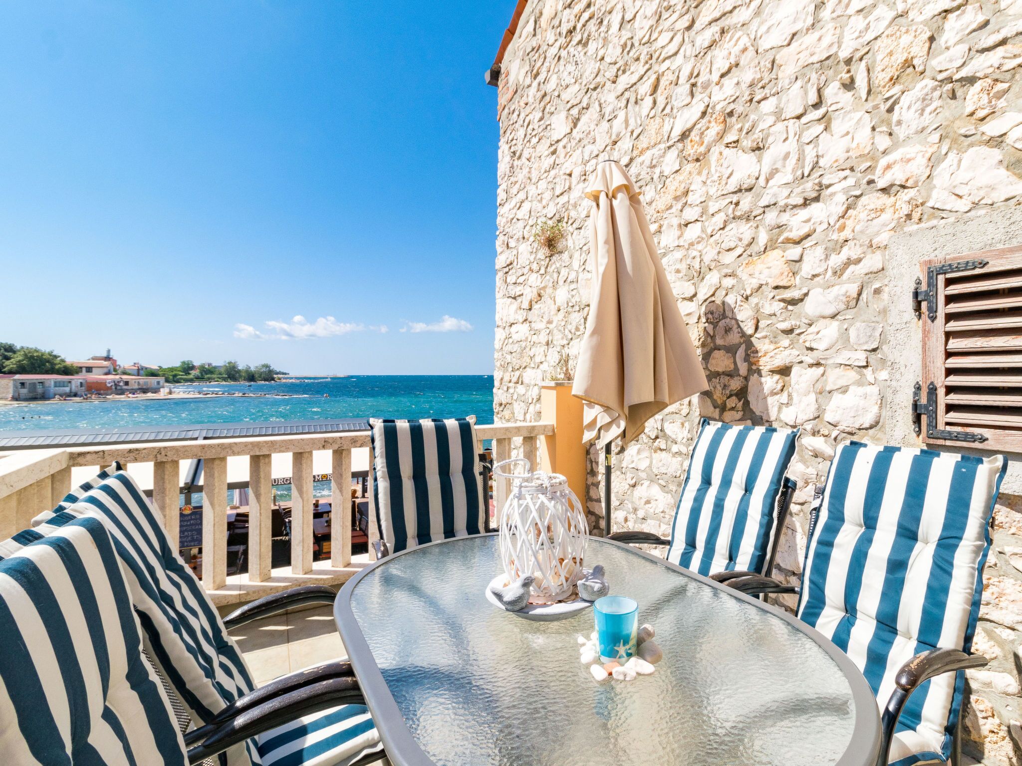 A terrace with a stone wall, striped cushions, and a table with a glass top.