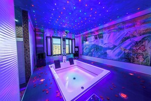 Un moderno spa con una bañera grande en el centro, un techo con luces de colores y un mural de mariposas en la pared.