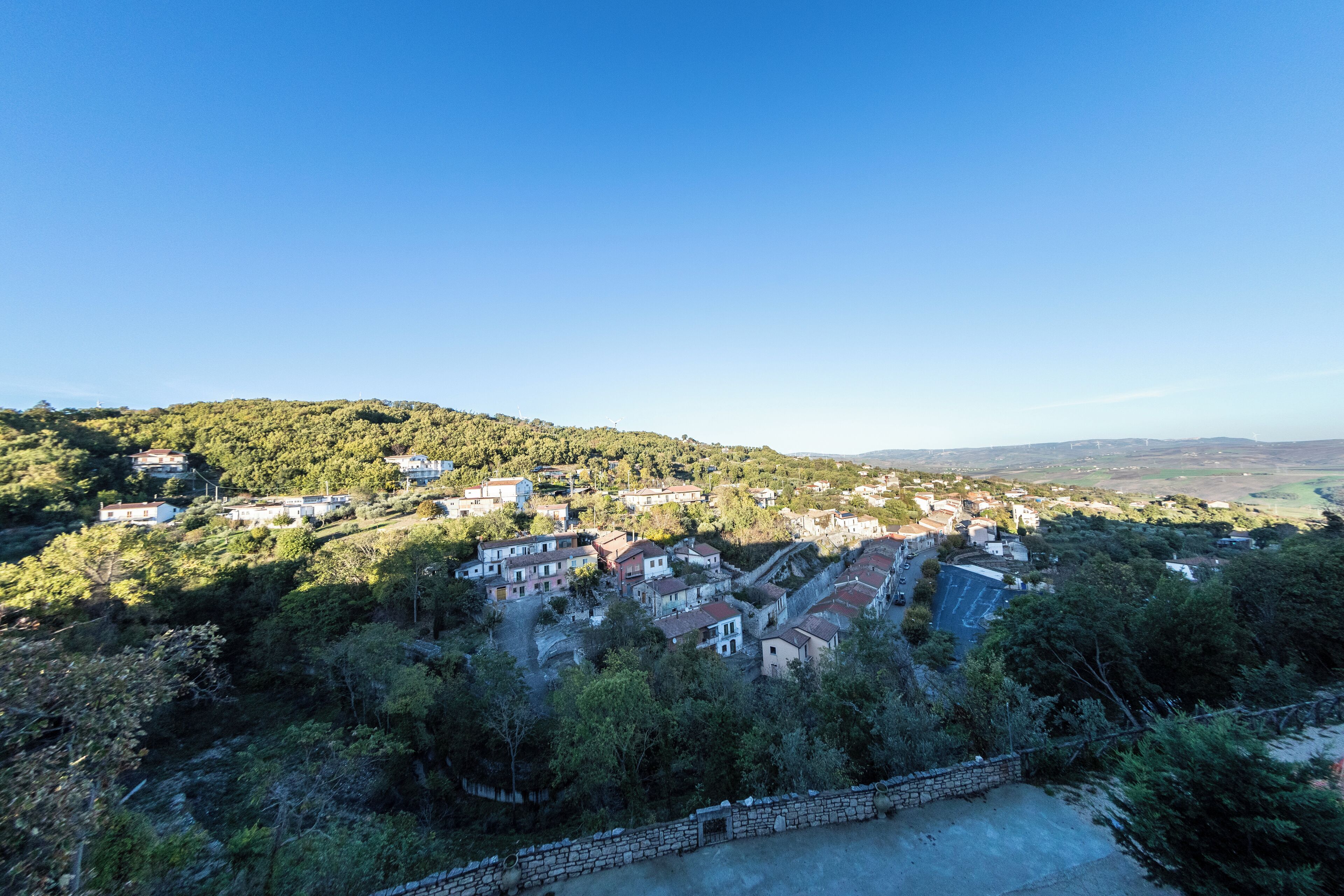 A hillside village with traditional houses, a stone wall, and a clear blue sky.