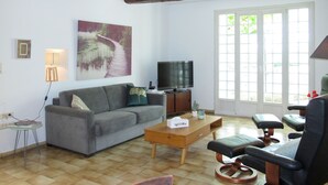 Un salon avec un canapé gris, une table basse en bois, un téléviseur et une fenêtre donnant sur un paysage verdoyant.