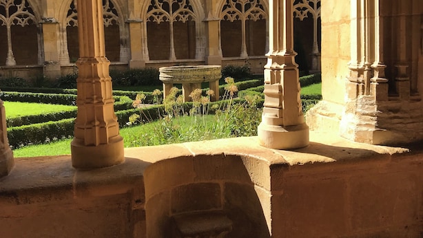Ein Innenhof mit gotischen Bögen und einem Brunnen, umgeben von einem gepflegten Garten.