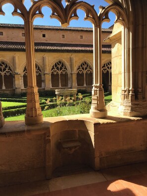 A courtyard with gothic arches and a fountain, surrounded by a well-maintained garden.