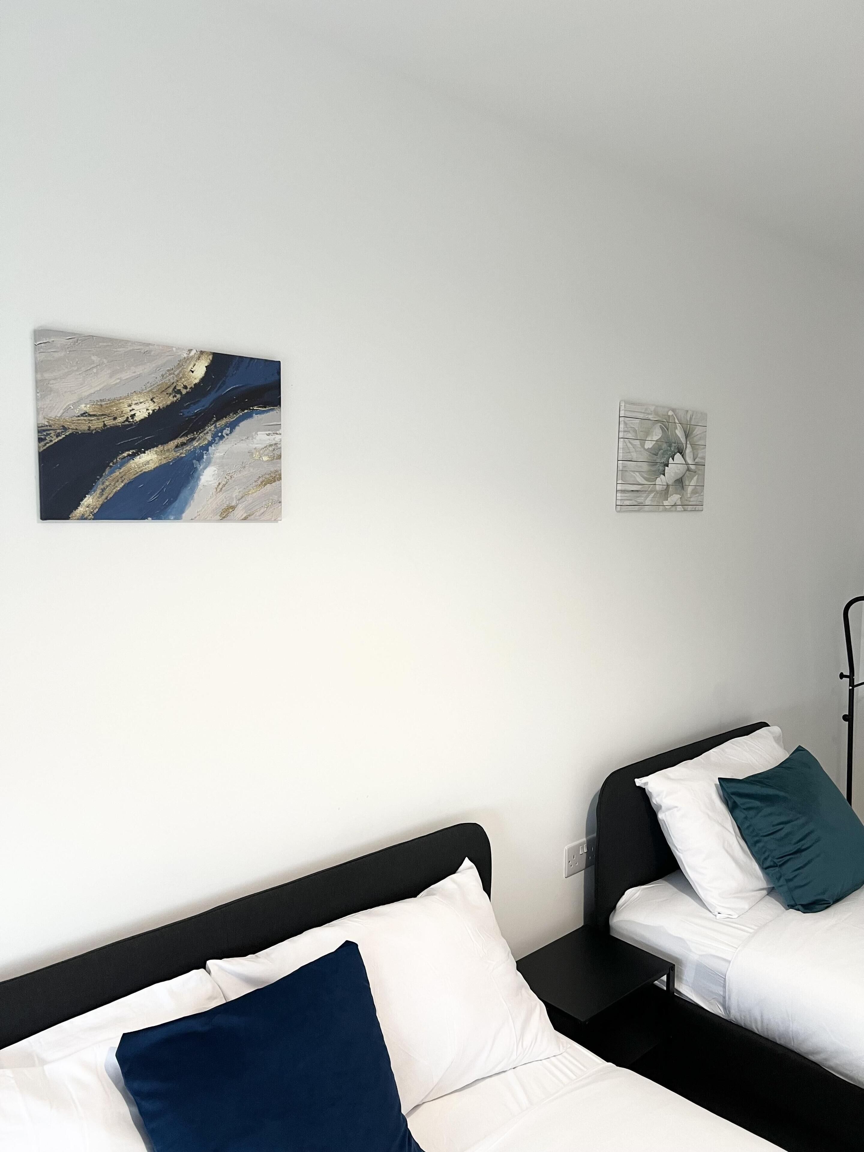 A hotel room with two beds, a nightstand, and two wall-mounted artworks.