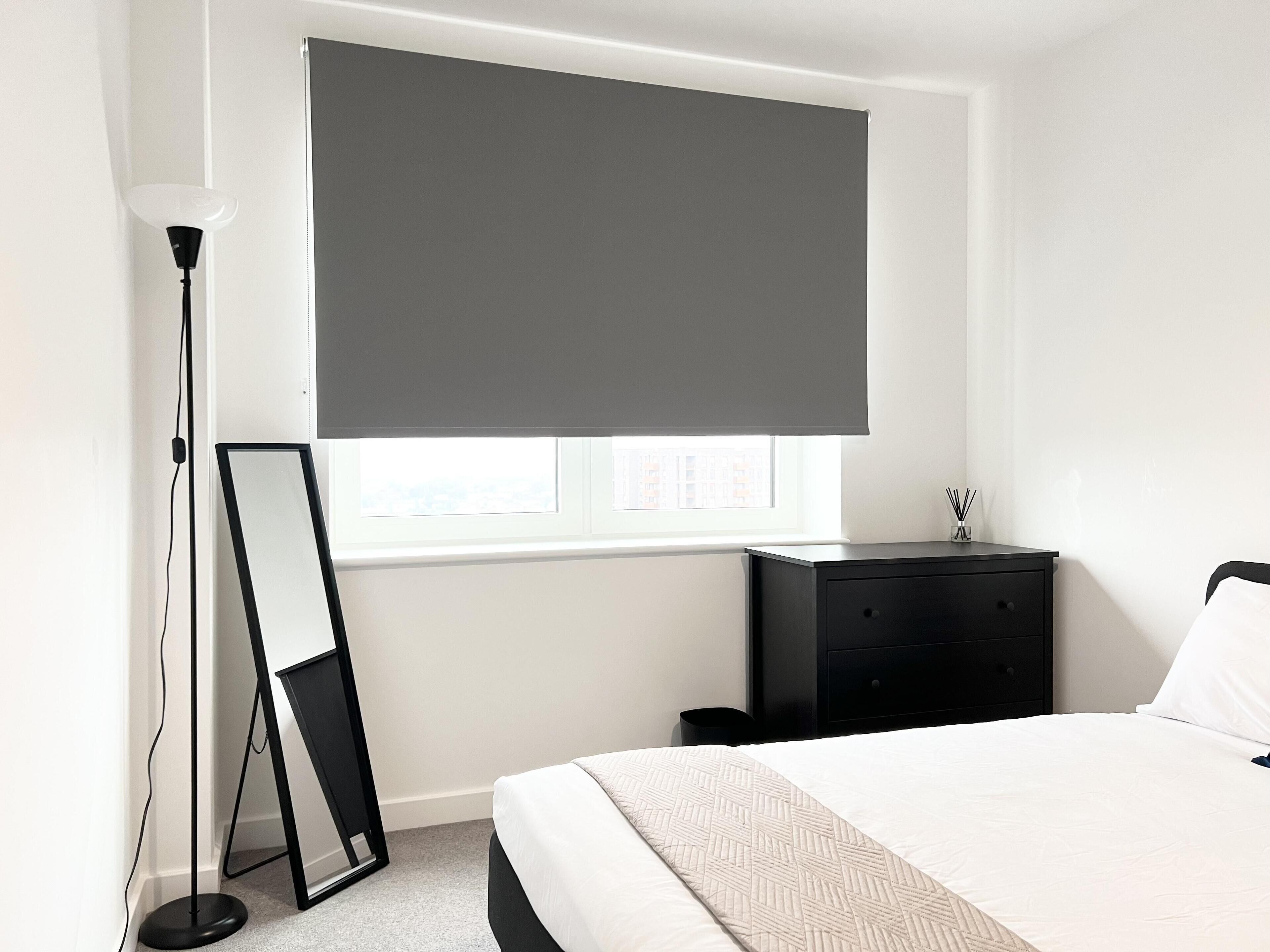A bedroom with a bed, a dresser, a floor lamp, and a window with a blind.