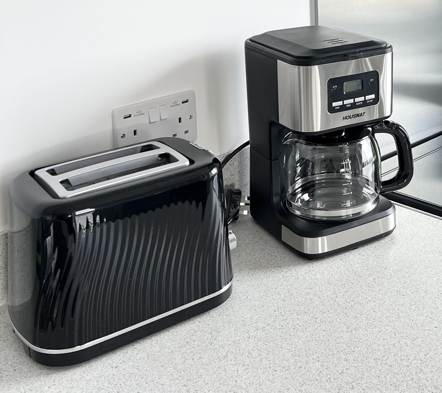A kitchen with a black toaster and a stainless steel coffee maker.