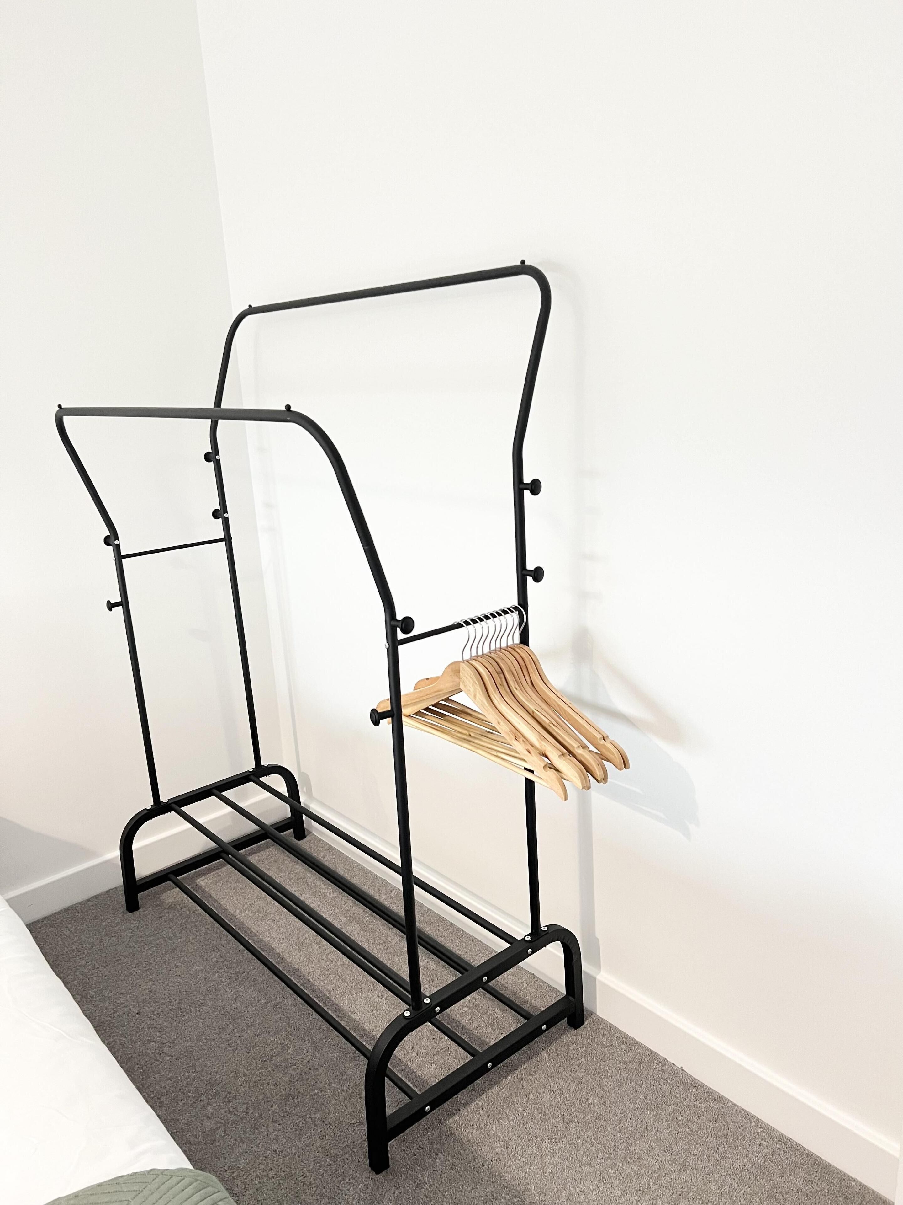 A black metal drying rack with wooden hangers against a white wall.