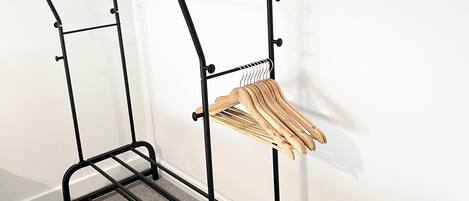 A black metal drying rack with wooden hangers against a white wall.