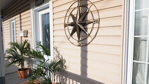 Exterior de una casa de madera con un adorno de brújula, plantas en macetas y un felpudo.