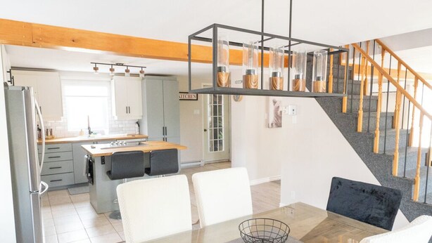 Una cocina moderna con armarios blancos, una isla de madera y un comedor con mesa de vidrio y sillas blancas.