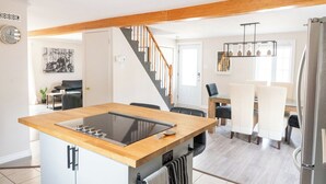 Una cocina moderna con una isla central, vigas de madera, una escalera, comedor y un refrigerador.
