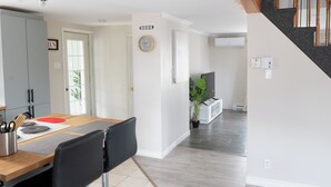 Una cocina moderna con armarios grises, una mesa de comedor de madera y una silla negra. Hay un reloj en la pared y una planta en maceta cerca de la entrada.