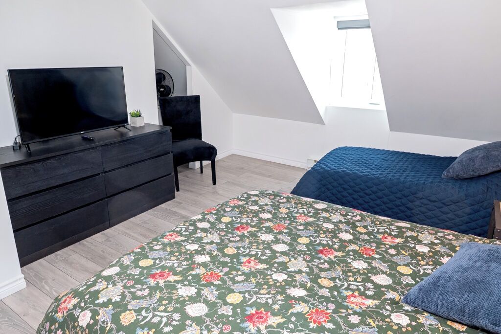 Une chambre avec une télévision, une commode, une chaise, un lit avec une couverture et une lucarne.